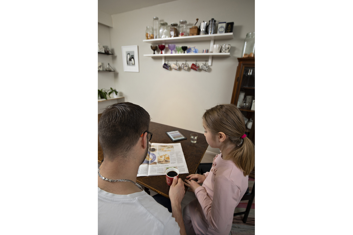 Isä ja lapsi lukevat sanomalehteä keittiön pöydän ääressä aamulla.