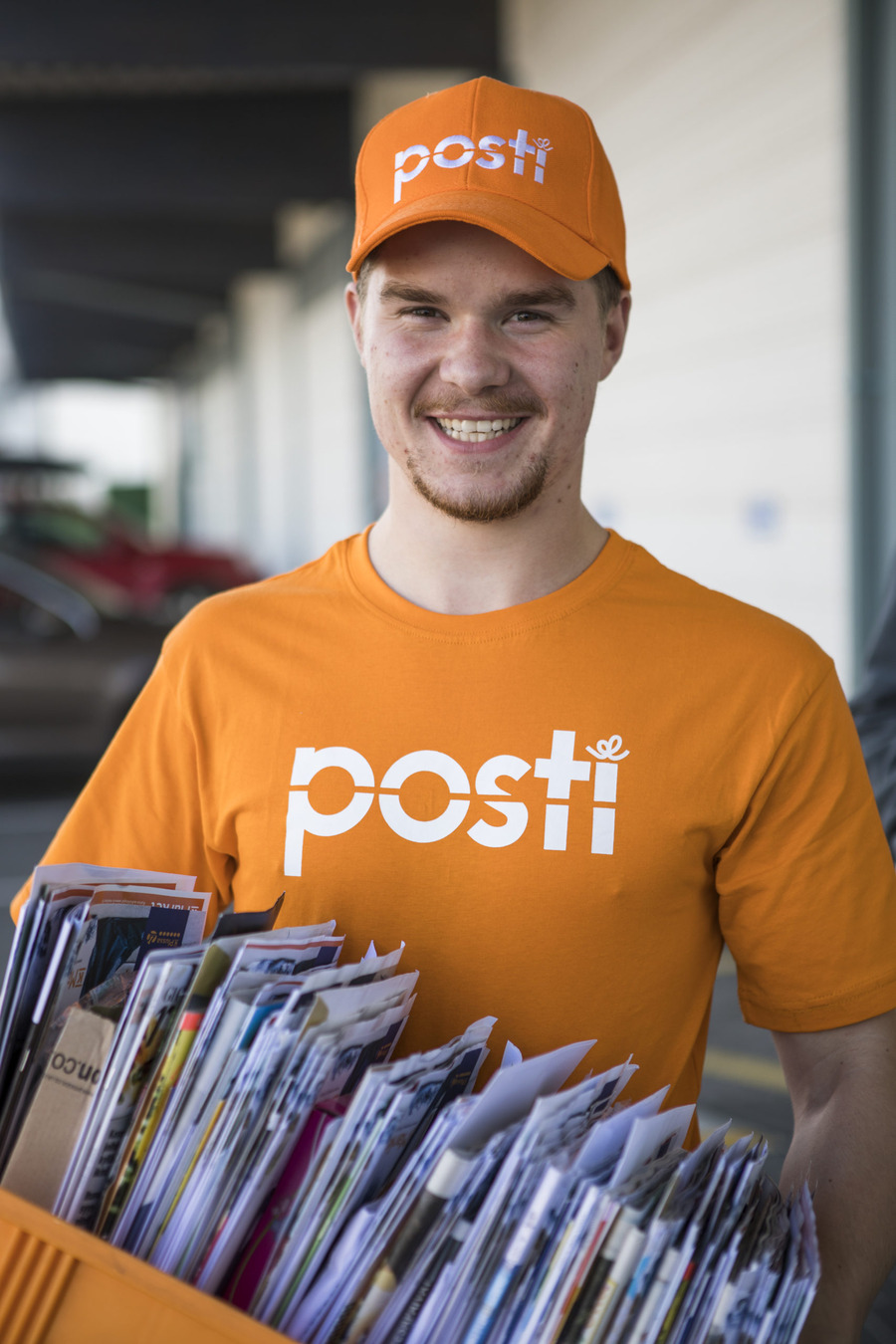 Postinkantaja kantamassa hymyillen laatikkoa, jossa on postia.