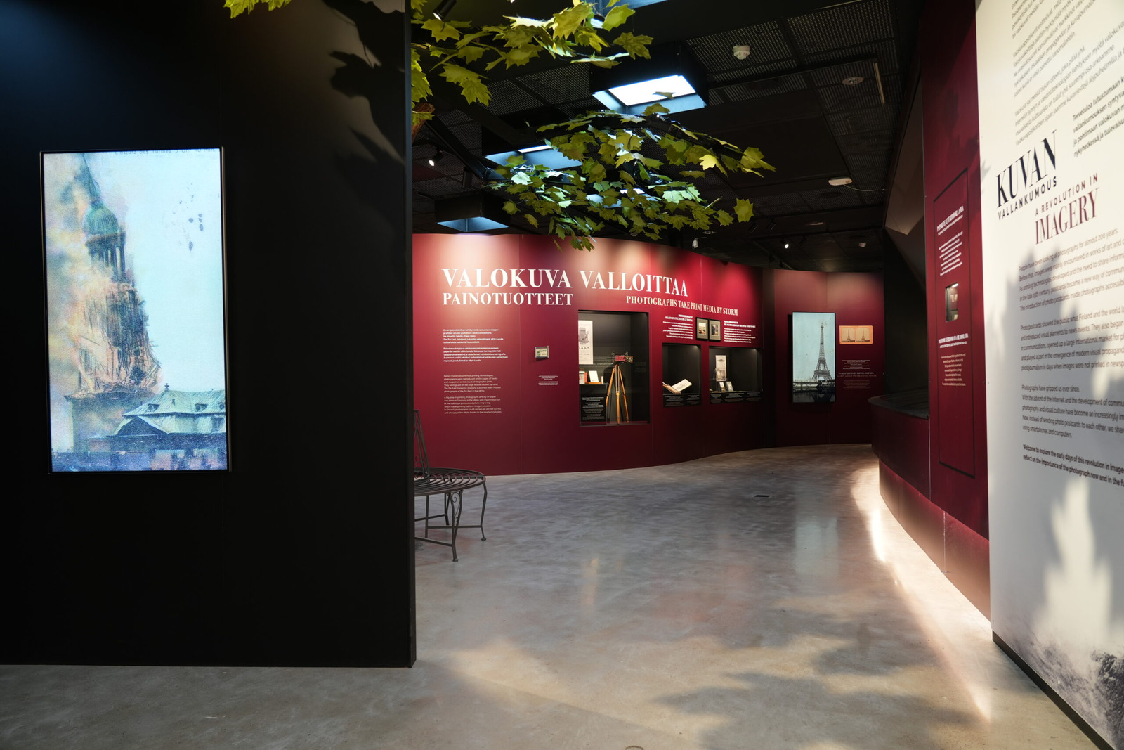 Näyttelytilan sisääntulo, jossa on vasemmalla sermiseinällä näyttö, jossa on kuva kirkon tornin palosta. Oikeanpuoleisella seinäpinnalla otsikkona Kuvan vallankumous A Revolution in imagenary sekä tekstiä. Kulkuaukosta avautuu näyttelytila, jossa on katossa vaahteranlehtiä, vasemman seinän takaa pilkistävä penkki ja kello kymmenestä kahteentoista kaartuvaa seinää teksteineen ja näyttelyesineineen. Otsikkona seinällä on Valokuva valloittaa Painotuotteet.