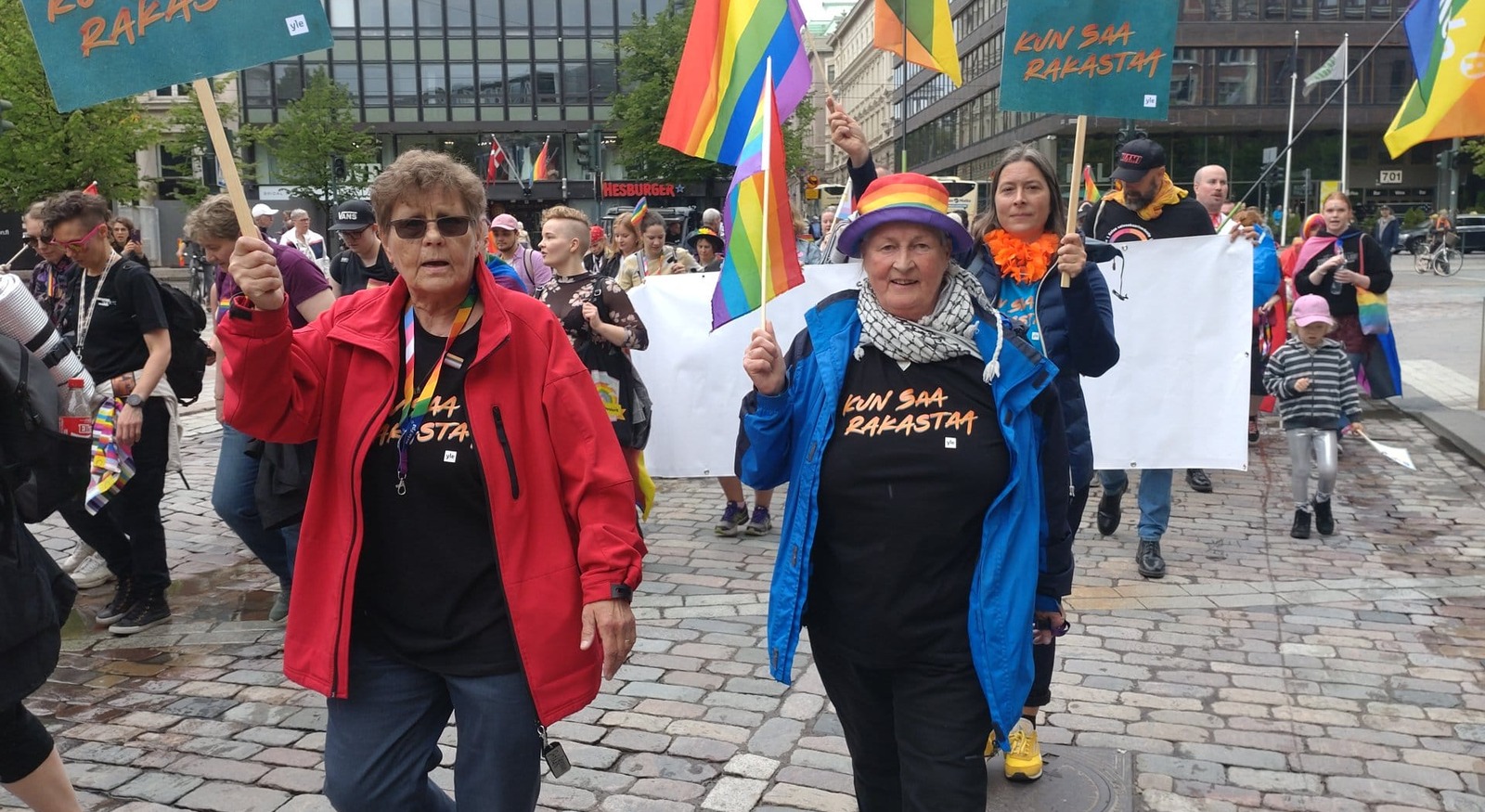 Kaksi ihmistä Pride-kulkueessa kyltit kädessään.