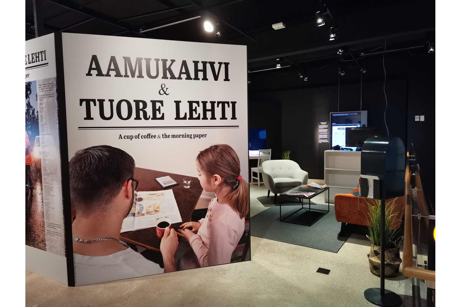 Näyttelytila, jossa iso kuva miehestä ja lapsesta lukemassa sanomalehteä.