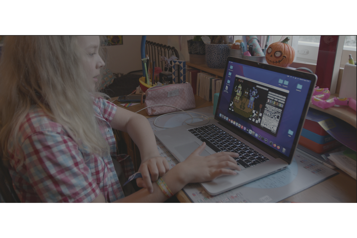 nuori pitkätukkainen tietokoneen äärellä pöydän ääressä.