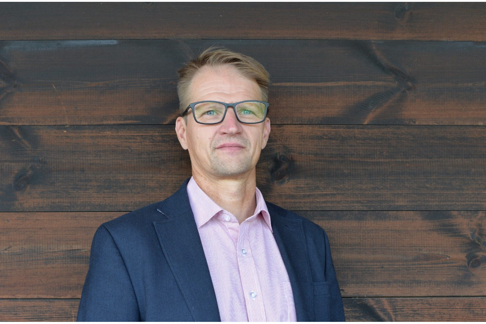 Vaaleahiuksinen ja silmälasipäinen mies kauluspaidassa ja puvun takissa.