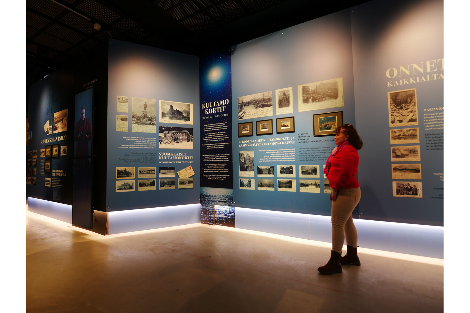 Postimuseon Kuvan vallankumous -näyttelyssä nainen katsoo seinämän postikortteja.