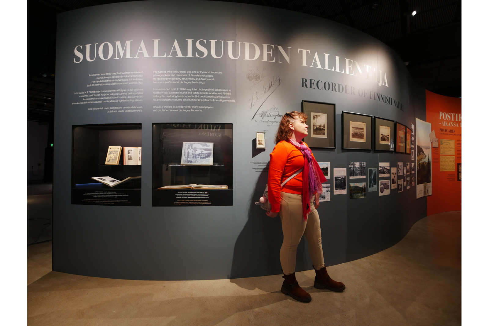 Nainen näyttelytilassa seinää vasten, jossa otsikkona Suomalaisuuden tallentaja.