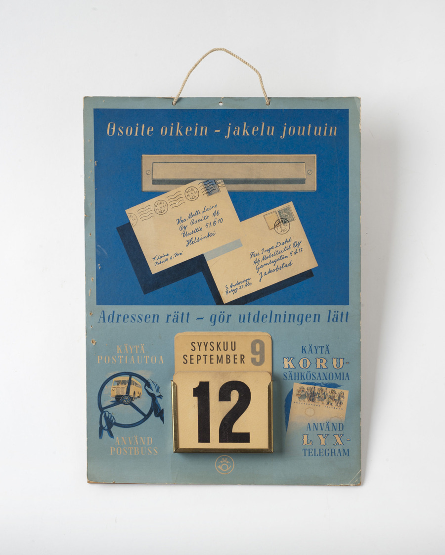 Suorakaiteenmuotoinen pahvilevy, jonka alareunassa nelikulmainen, yläreunasta avoin metallikehys. Kehykseen pujotettu kahden kokoisia nelikulmaisia pahvilappuja. Pienemmissä lapuissa numerot 1-31, päivämäärä. Isommissa lapuissa kuukaudet, yksi lappu puuttuu. Päivyrin taustalevy väriltään vaaleansininen. Sen yläosassa tummemman sininen neliö, jonka sisällä kuva postiluukusta ja kahdesta kirjekuoresta. Kirjeet päivätty 16.5.54 ja 7.6.54. Taustassa teksti Osoite oikein - jakelu joutuin adressen rätt - gör utdelningen lätt käytä postiautoa använd postbuss käytä korusähkösanomia använd lyxtelegram.