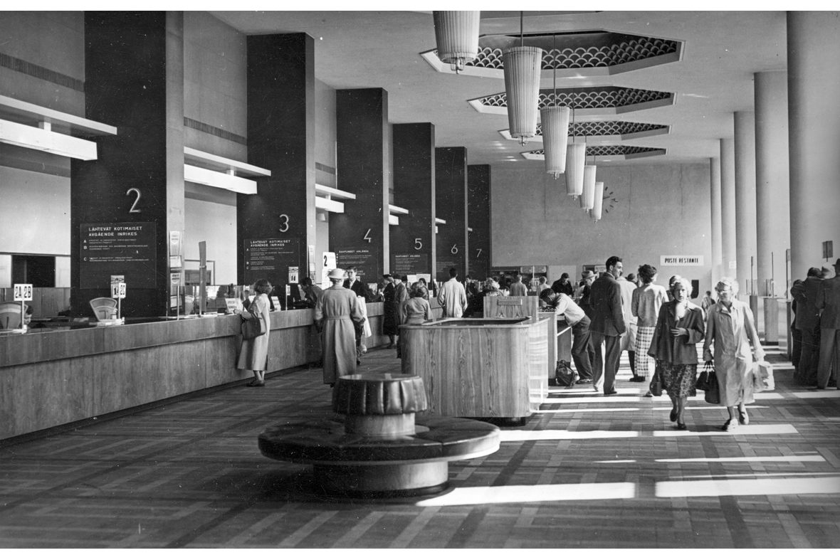 Mustavalkoisessa kuvassa Helsingin Pääpostin asiakaspalveluaulassa asiakaspalvelua eri pisteillä ja ihmisiä liikkumassa.