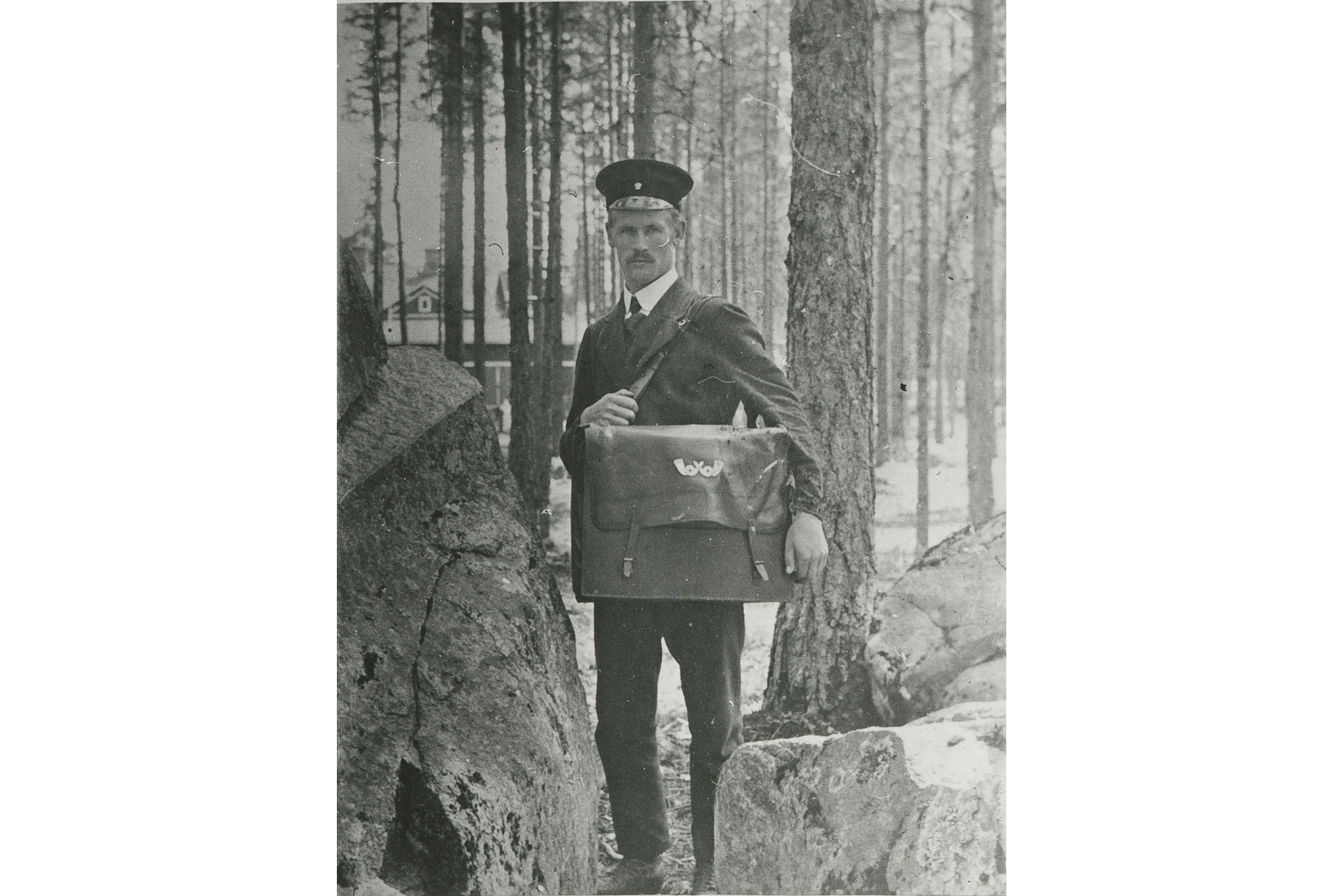 Postiljooni Kalle Saviaho ison postilaukkunsa kanssa. Uusien pukumääräysten myötä vuonna 1904 puvut alkoivat muistuttaa arkipukuja. Perusvärinä oli tummanvihreä verka. Päällystakki oli tummanharmaa. Pukujen hankintaan saatiin avustusta.