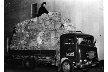 vanha kuorma-auto, jossa iso kasa postisäkkejä kyydissä ja niiden päällä henkilö.