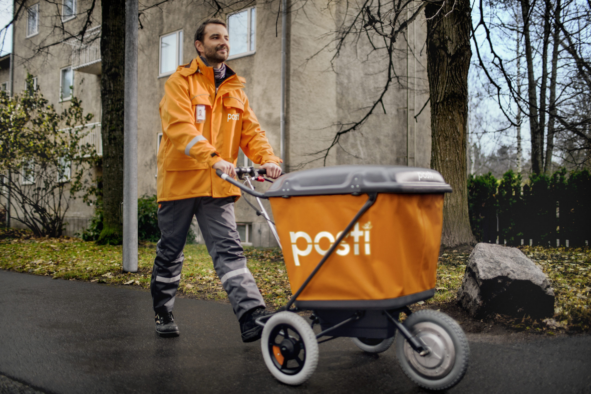 Postinjakaja kuljettamassa jakelukärryä kävelytiellä syksyn märkyydessä.
