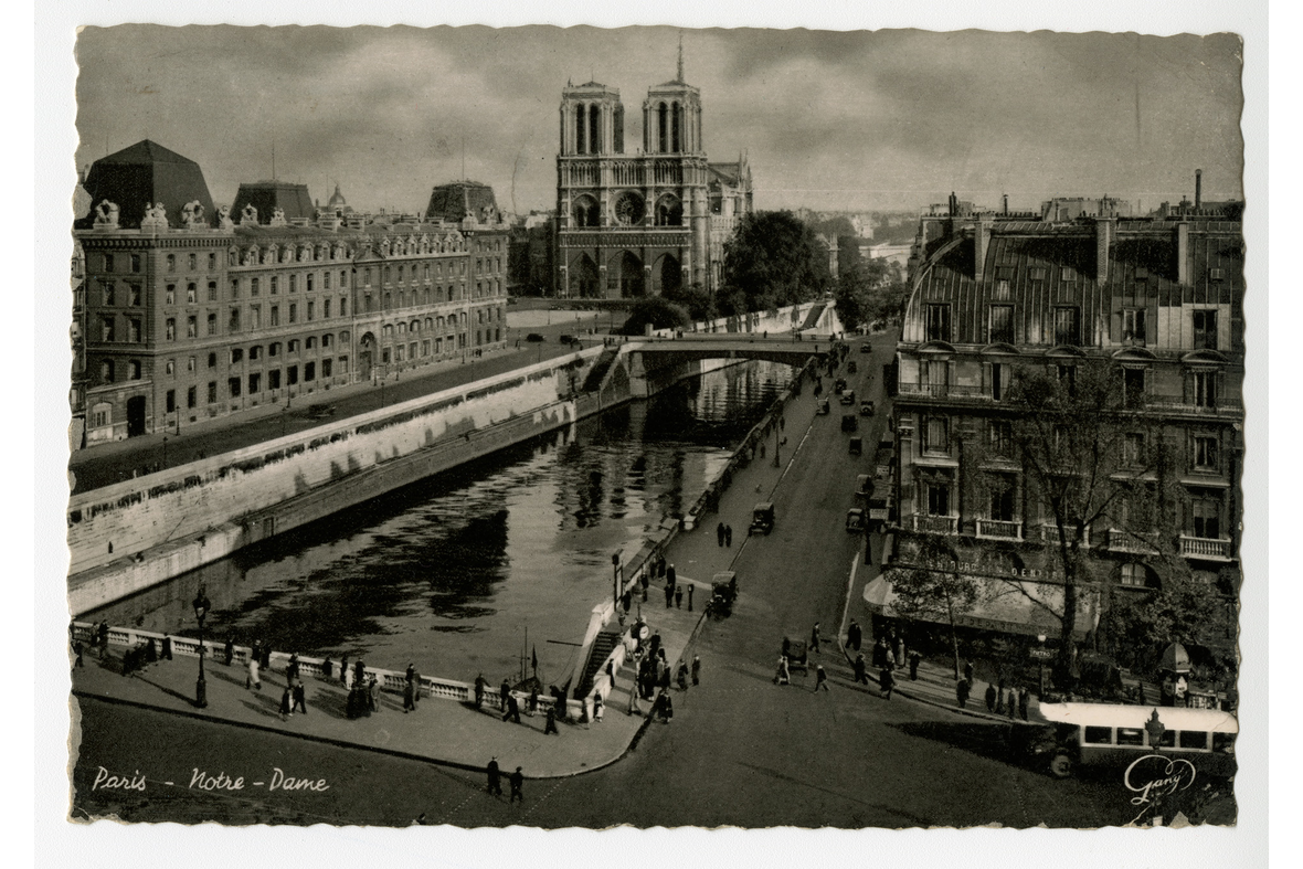 Vaakatasoinen postikortti, jossa on mustavalkoinen kuva kaupungista katuineen, ihmisvilinöineen ja kerrostaloineen, keskellä takana kirkko, jonka vieressä keskellä kulkevan joen ylittävä silta. Vasemmassa alalaidassa teksti kaunolla Paris - Notre-Dame.