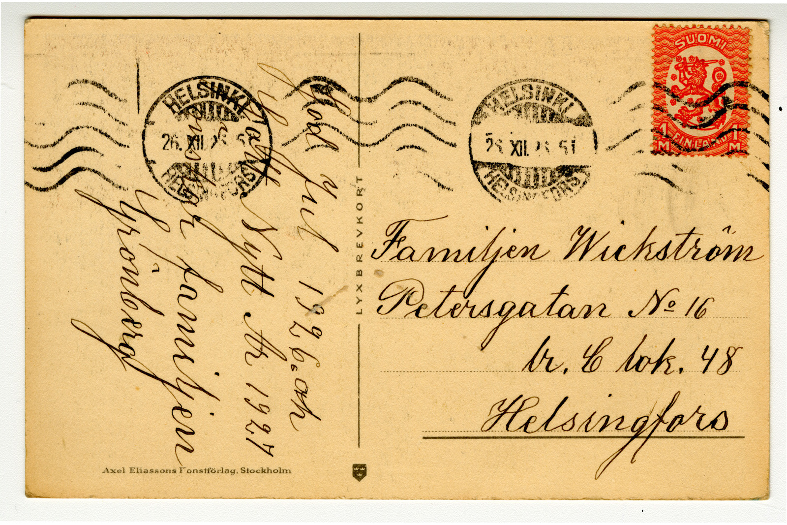 Postikortin tausta, jossa on punainen Vaasan malli 1918 -postimerkki Helsingin postileimoilla, sivuttain kirjoitettu joulutoivotus ja osoite-kohdassa Familjen Wickströmin osoite Helsinforsiin.