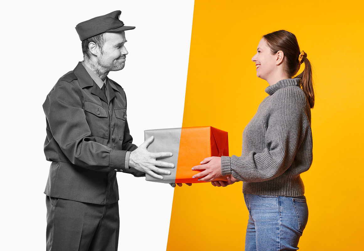 Vanhan ajan postinjakaja mustavalkoisessa osuudessa ojentaa paketin nuorelle naiselle nykyaikaan värilliseen kuvaosuuteen.