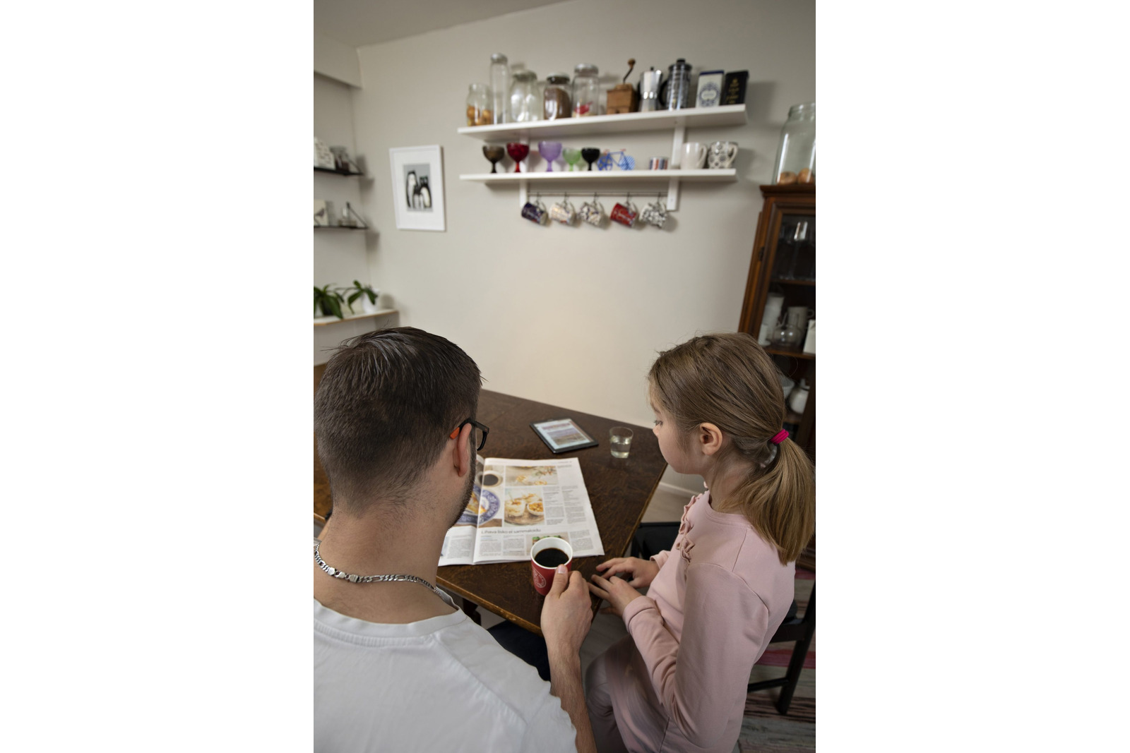En man och en flicka läser en tidning vid köksbordet.