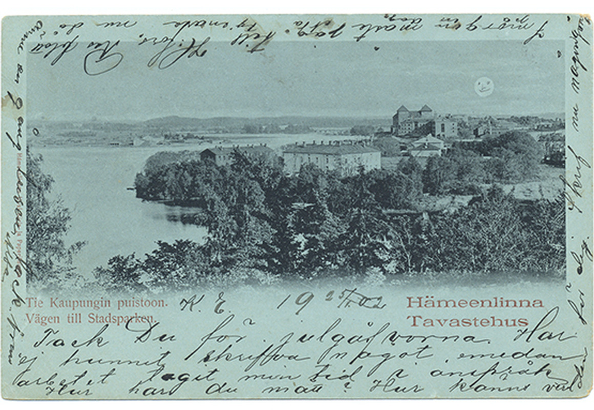 Siniselle kartongille mustasävyisenä painetussa postikortissa on Hämeen linna 1900-luvun alussa. Edustalla puustoa ja maisemassa vesistöä.
