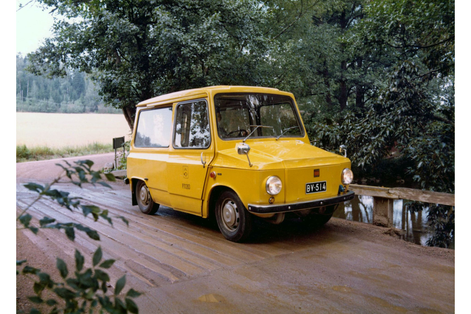 Keltainen postiauto puisella maantiesillalla.