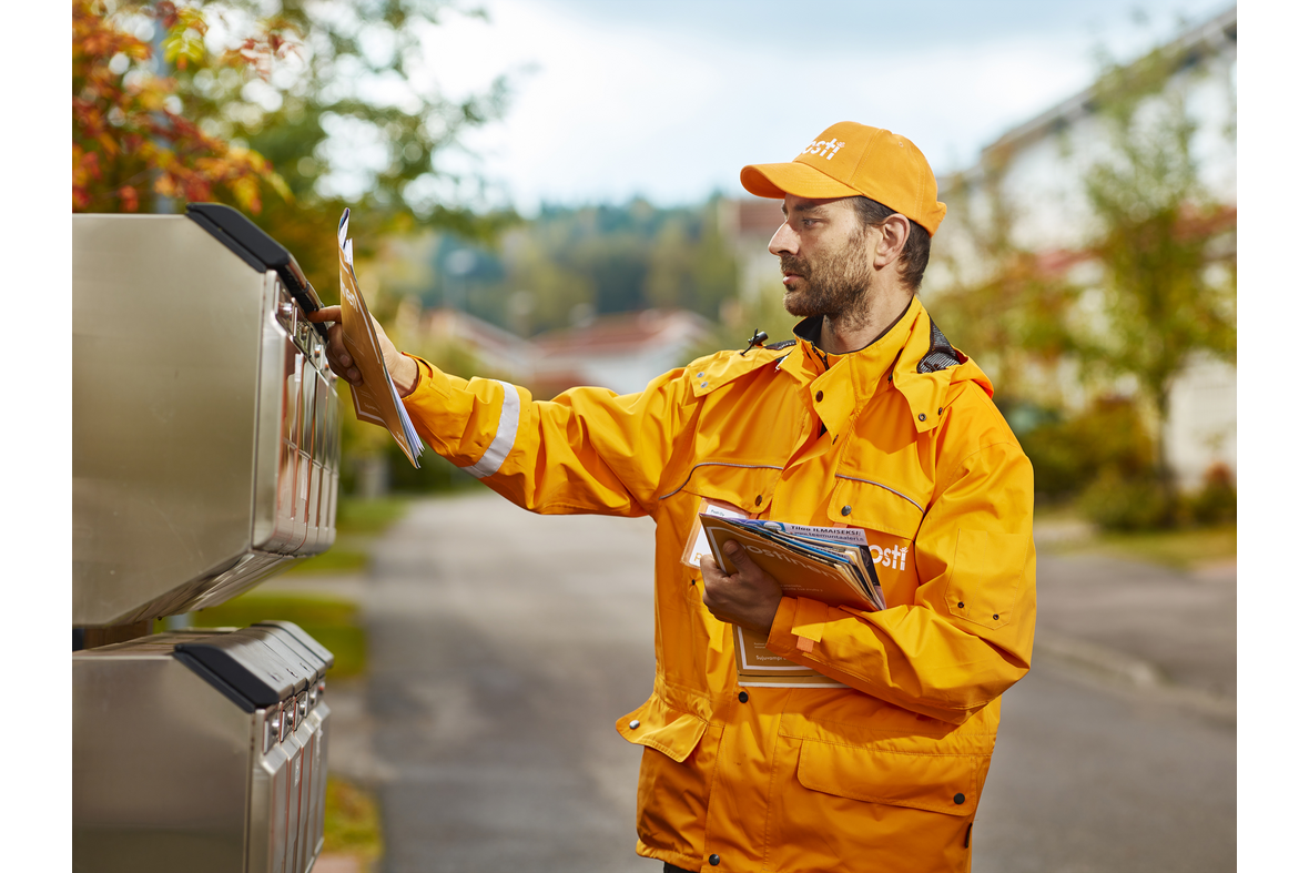 Postinjakaja laittamassa postilaatikkoon kaksirivisessä postilaatikkoryhmässä.