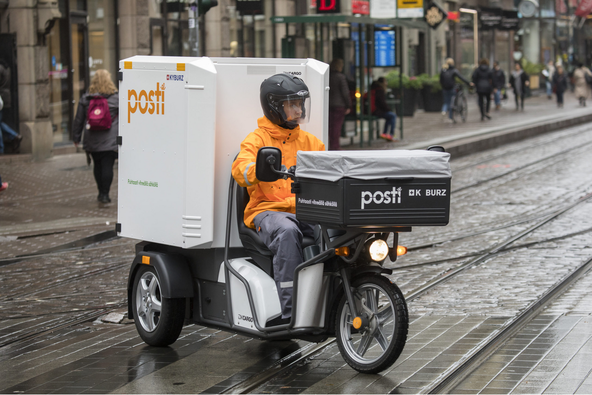 Postinjakaja ajamassa sähkörahtiskootteria raitiotien yli suojatien kohdalla märällä kelillä.