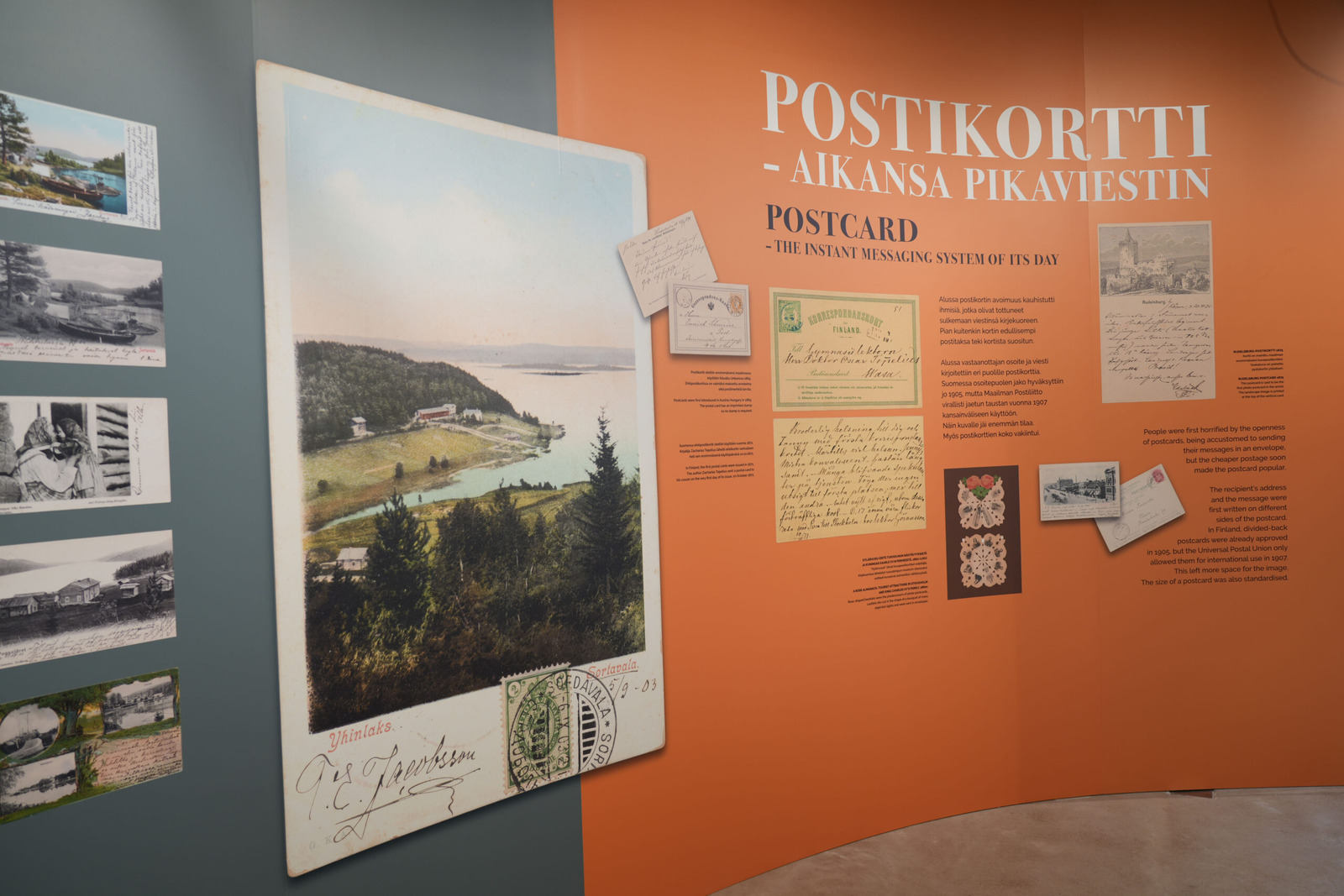 Seinämällä on kuvia postikorteista ja tekstiä. Otsikkona on Postikortti - aikansa pikaviestin.