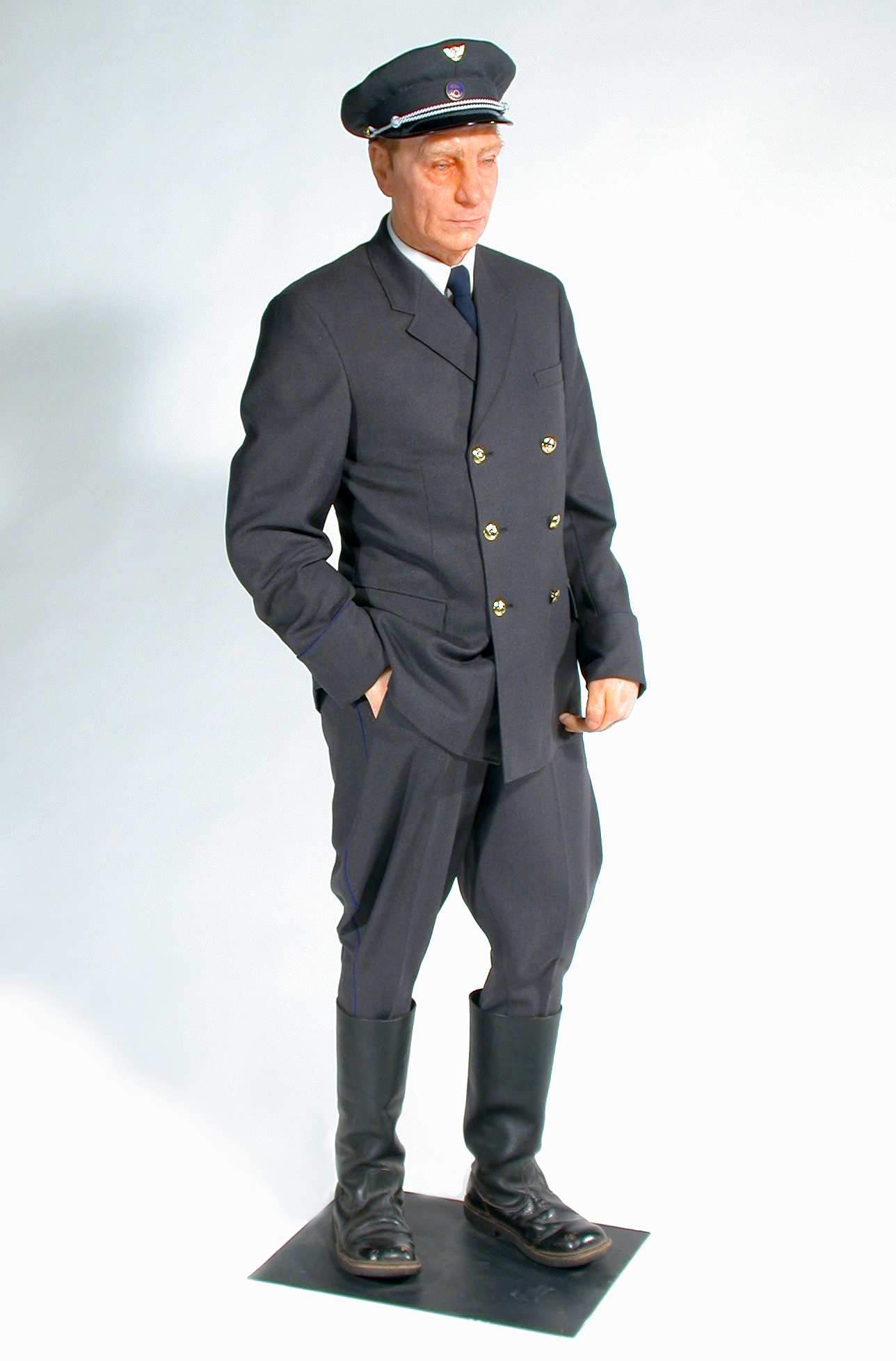 Mallinukke, jolla on päällään harmaa virkapuku kaksirivinapituksen takilla, housuilla ja lakilla.