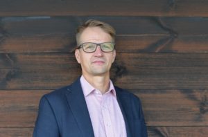 Vaaleahiuksinen ja silmälasipäinen mies kauluspaidassa ja puvun takissa.