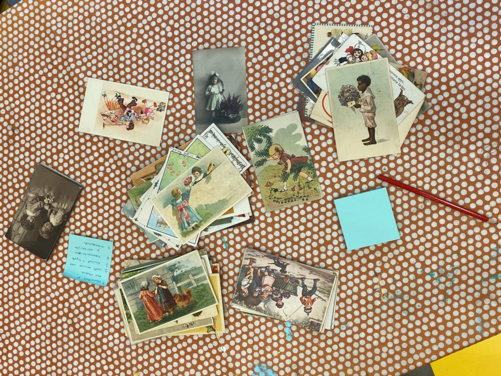 Pöydällä postikortteja, joiden kuva-aiheena lapset. Kortteja lajiteltu ryhmiin kuvien perusteella.