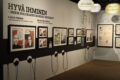 Näyttelytilassa kuvia seinällä ja kuulokkeita, joista voi kuunnella näyttelyn sisältöjä.