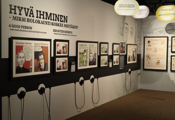 Näyttelytilassa kuvia seinällä ja kuulokkeita, joista voi kuunnella näyttelyn sisältöjä.
