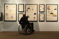 Pyörätuolissa istuva mies katselee näyttelyä.