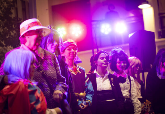 Kuvassa cosplay-näytöksen osallistujat seisovat rivissä. Taustalla on violetti ja punainen valo.