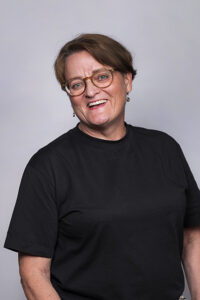 Silmälasipäinen, hymyilevä nainen mustassa t-paidassa henkilökuvassa.