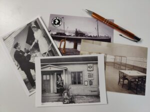 Neljä mustavalkoista postiaiheista postikorttia ja mustekynä valkoisella taustalla.