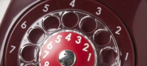 Lähikuva punaisesta esineestä, jossa on pyöreä, kierrettävä numerovalitsin. Tunnistatko? Kyseessä on vanha lankapuhelin.