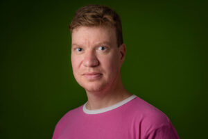 Keski-ikäinen, lyhyttukkainen mies vaaleanpunaisessa paidassa.