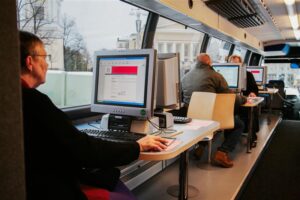 Ihmisiä tietokoneiden äärellä linja-autossa.