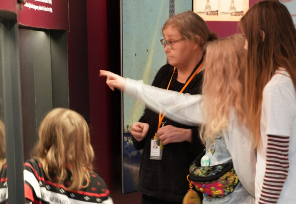 lapsia katsomassa näyttelyä oppaan kanssa.