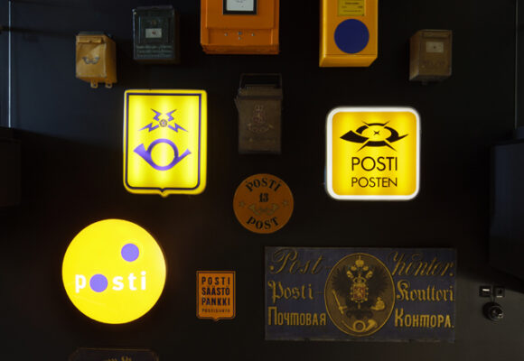 erilaisia postin kylttejä joissa erilaisia Postin logoja seinällä