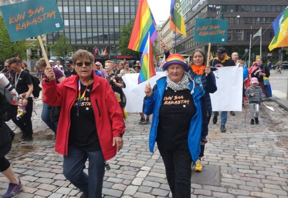 Kaksi ihmistä Pride-kulkueessa kyltit kädessään.