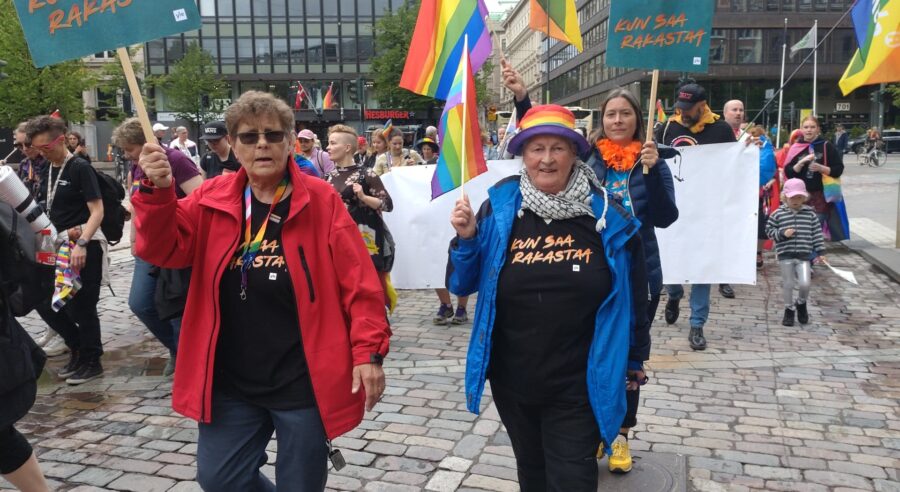 Kaksi ihmistä Pride-kulkueessa kyltit kädessään.
