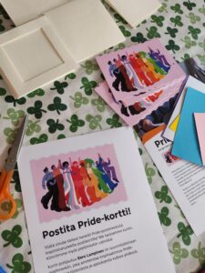 Pöydällä kortteja ja paperi jossa lukee Postita Pride-kortti.